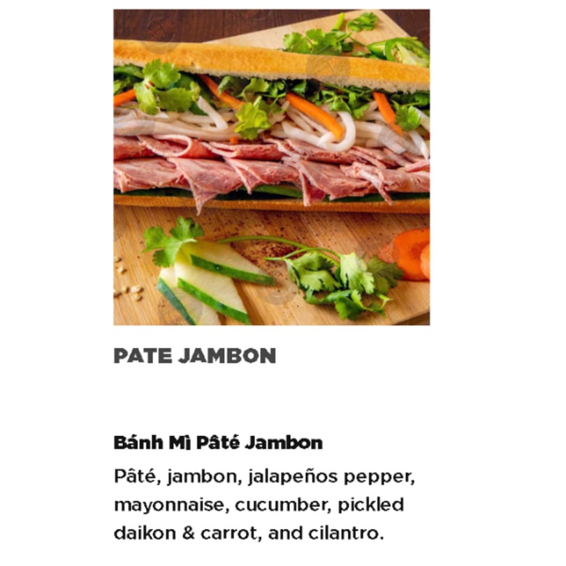 A close-up of a Vietnamese Bánh Mì Pâté Jambon sandwich with ham, vegetables, and cilantro.