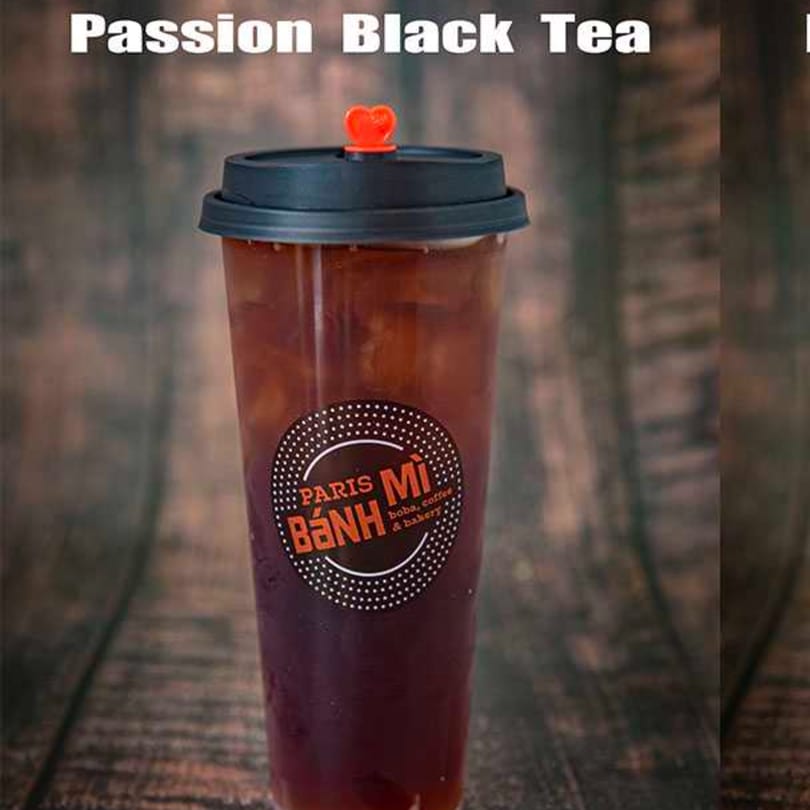 A clear plastic cup of Paris Banh Mi Passion Black Tea with a black lid and red heart stopper.