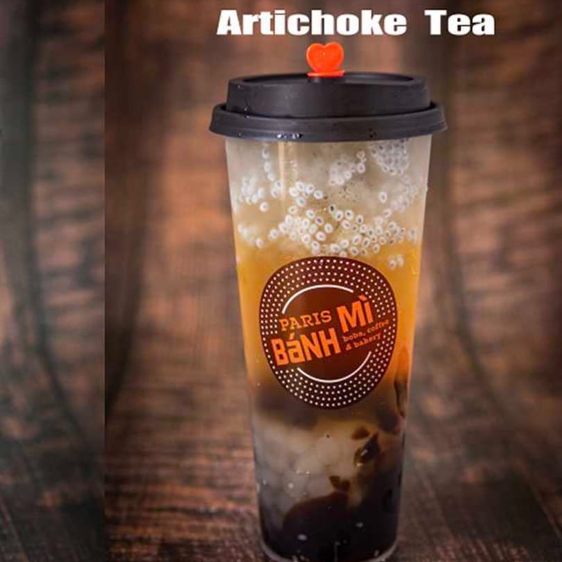 Paris Banh Mi Artichoke Tea with boba and a heart-shaped stopper on a wooden background.