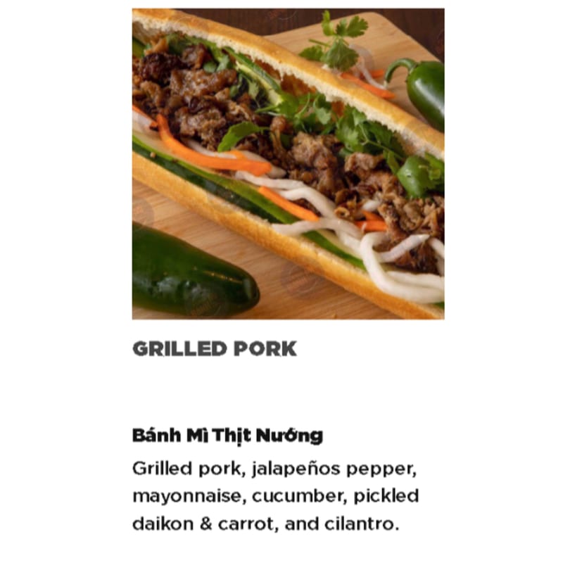 A grilled pork Banh Mi sandwich with cilantro, pickled vegetables, and a jalapeño on a cutting board.