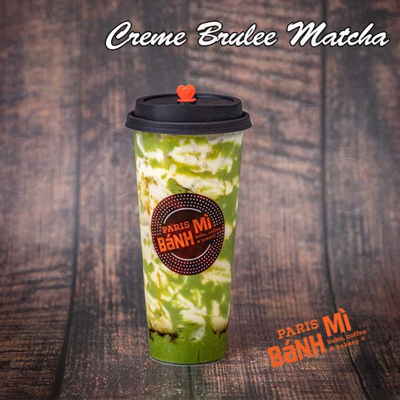 A Paris Banh Mi Creme Brulee Matcha drink with green and white layers, a black lid, and a red heart stopper.