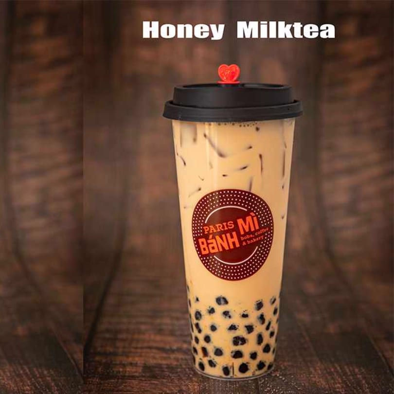 Honey Milk Tea with tapioca pearls and ice in a clear cup with a Paris Banh Mi logo.