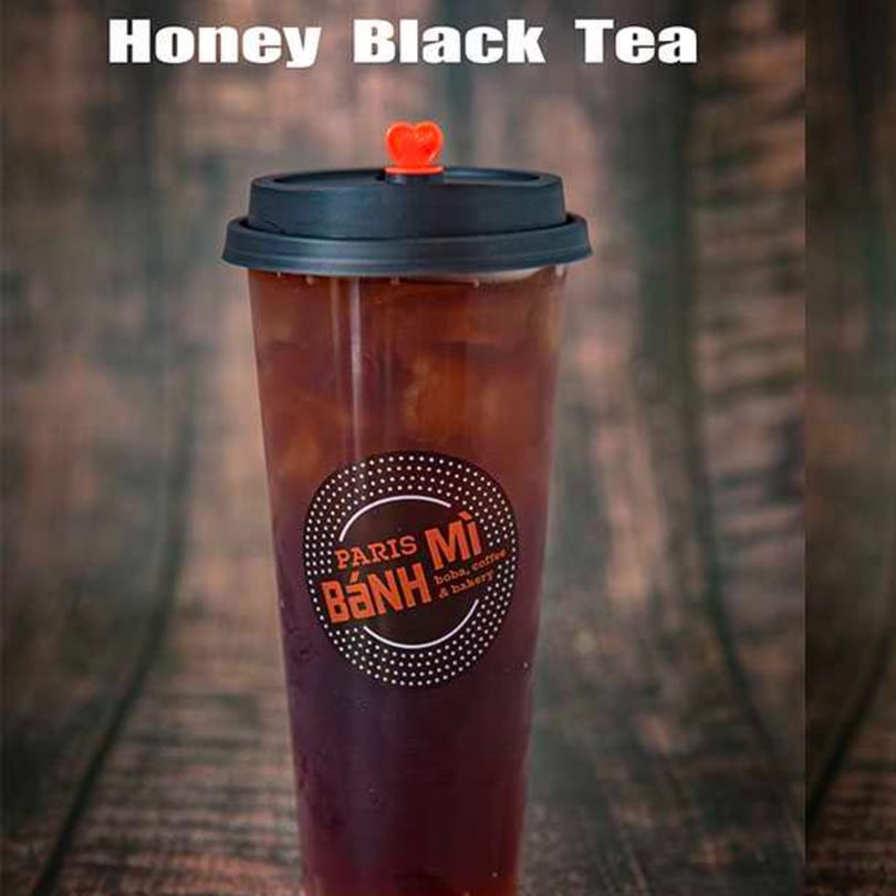 Honey Black Tea from Paris Banh Mi, a dark iced beverage in a clear cup with a black lid.