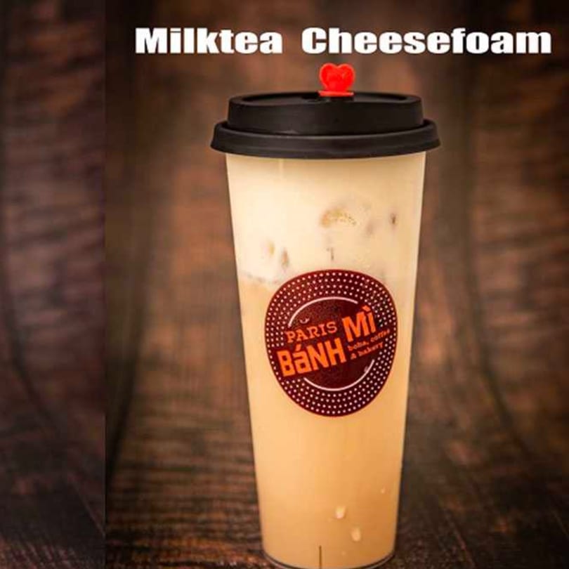 Paris Banh Mi milk tea with cheese foam, topped with a red heart, on a wooden table.