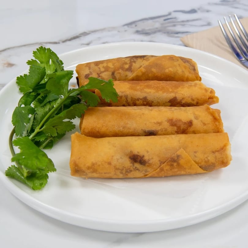 Four crispy Vietnamese spring rolls with fresh cilantro on a white plate.