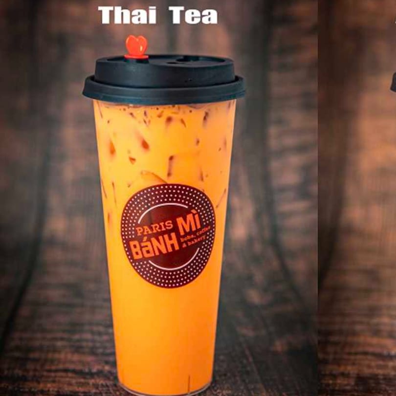 Iced Thai Tea in a clear plastic cup with a black lid and red heart stopper.