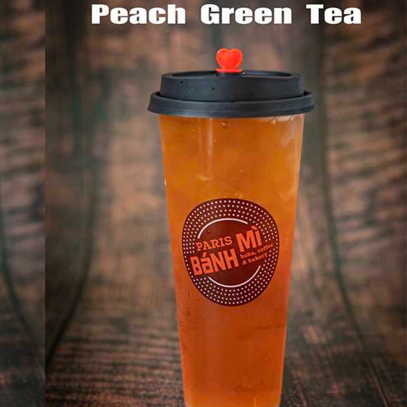 Peach Green Tea from Paris Banh Mi in a clear cup with a black lid and red heart stopper.