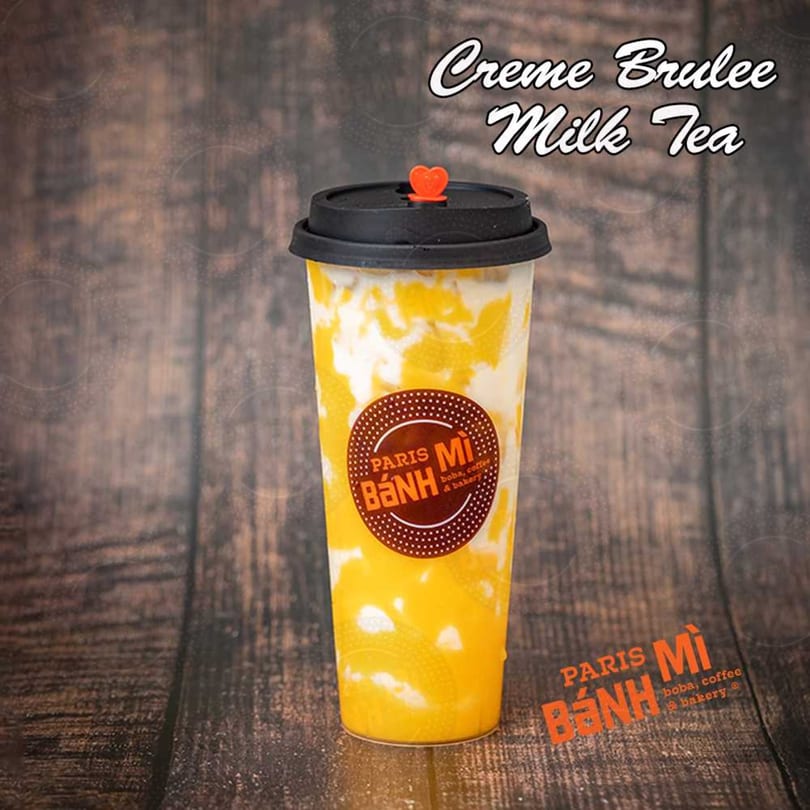 A Paris Banh Mi Creme Brulee Milk Tea with a heart-shaped straw stopper on a wooden background.