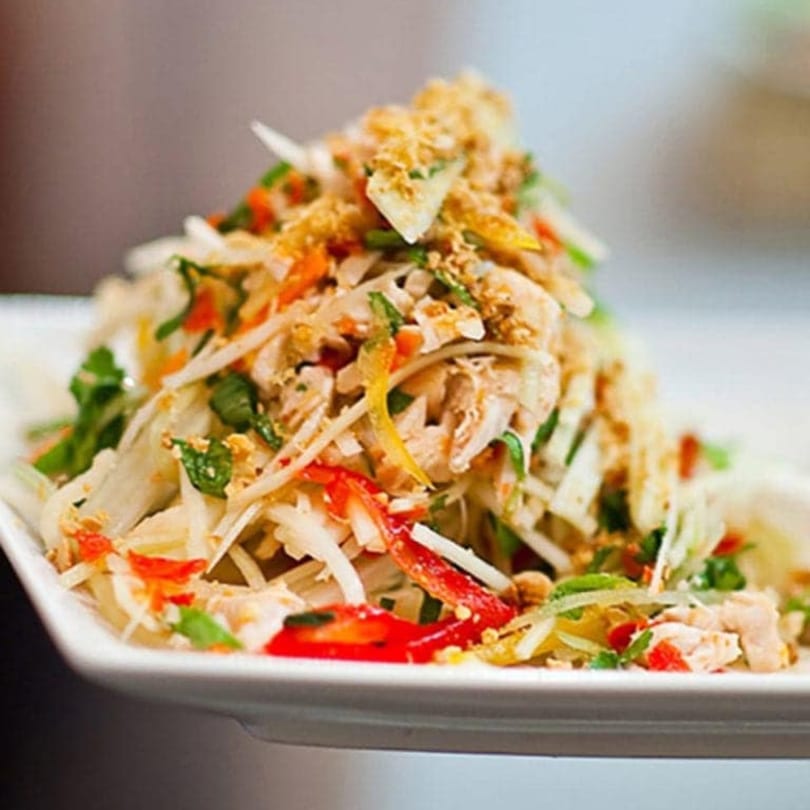Vietnamese chicken salad with shredded cabbage, carrots, herbs, and crushed peanuts on a white plate.