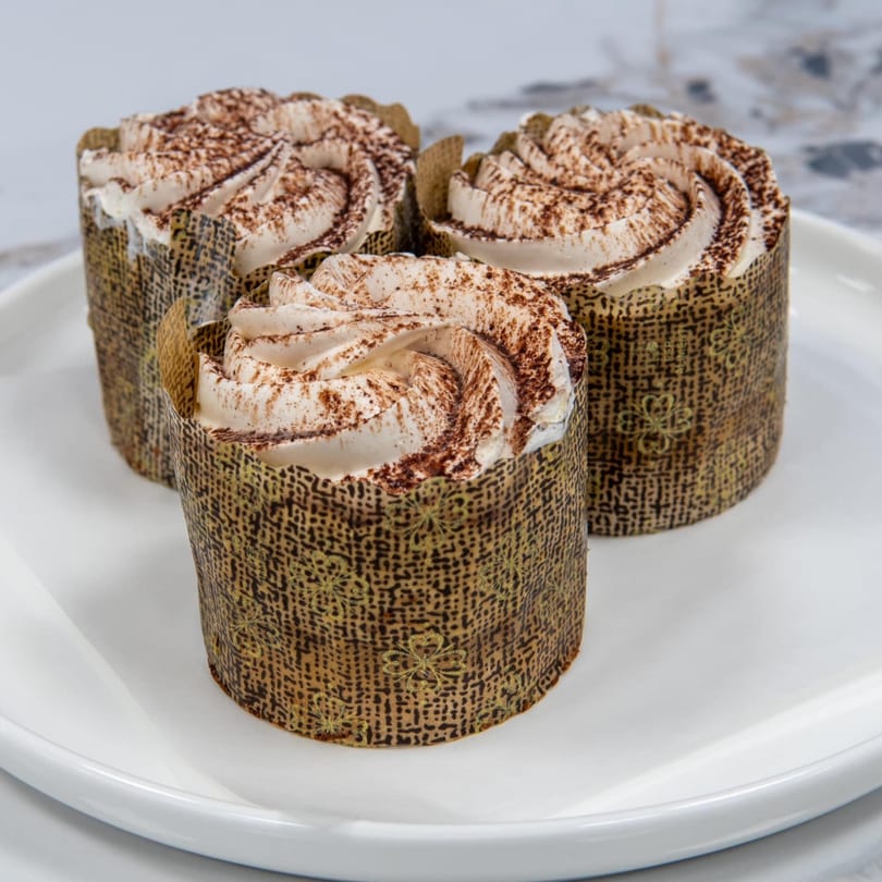 Three tiramisu cupcakes with whipped cream and cocoa powder on a white plate.