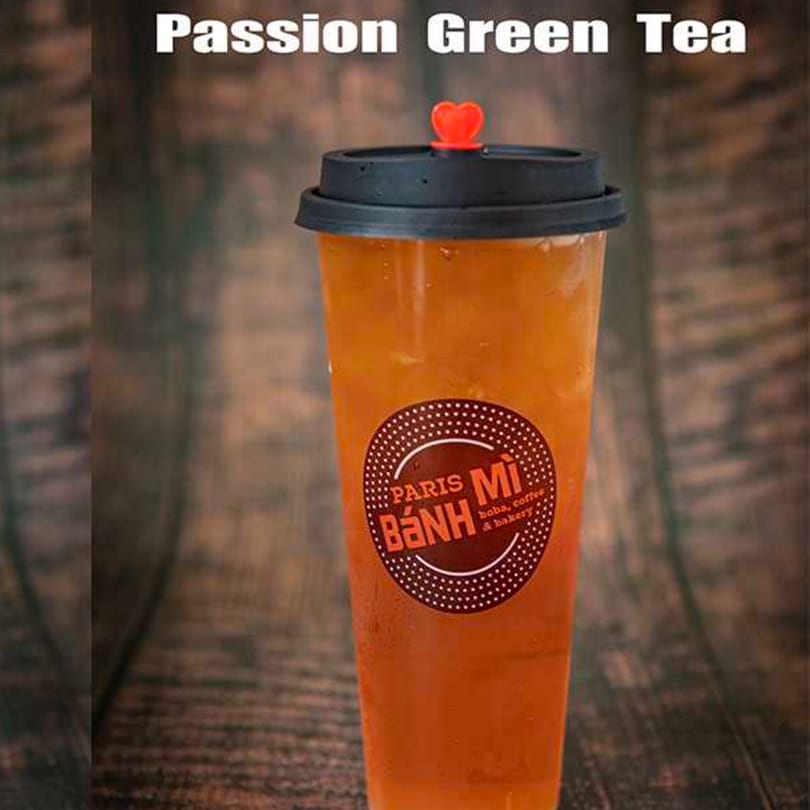 A tall plastic cup of Paris Banh Mi's Passion Green Tea with a heart-shaped stopper.