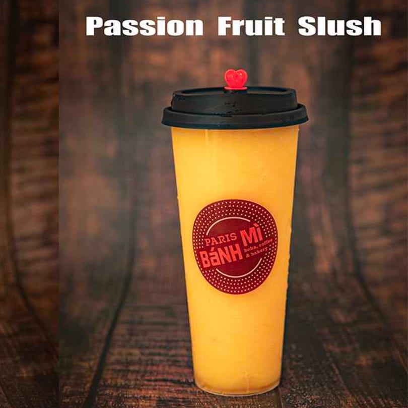 A tall cup of yellow passion fruit slush with a red Paris Banh Mi logo.
