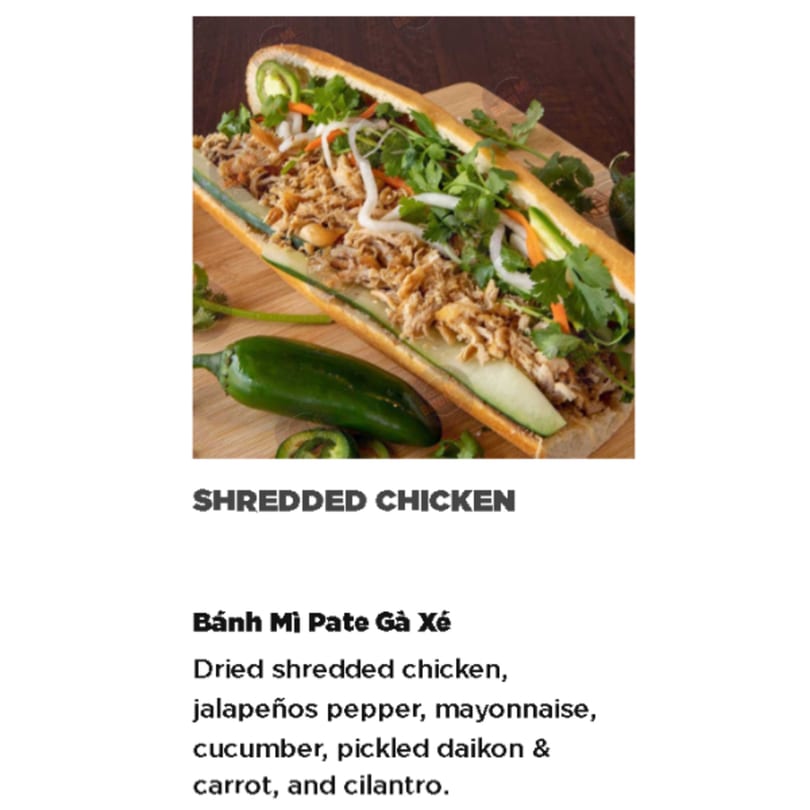 A Shredded Chicken Banh Mi with jalapeños, cucumber, and cilantro on a wooden board.