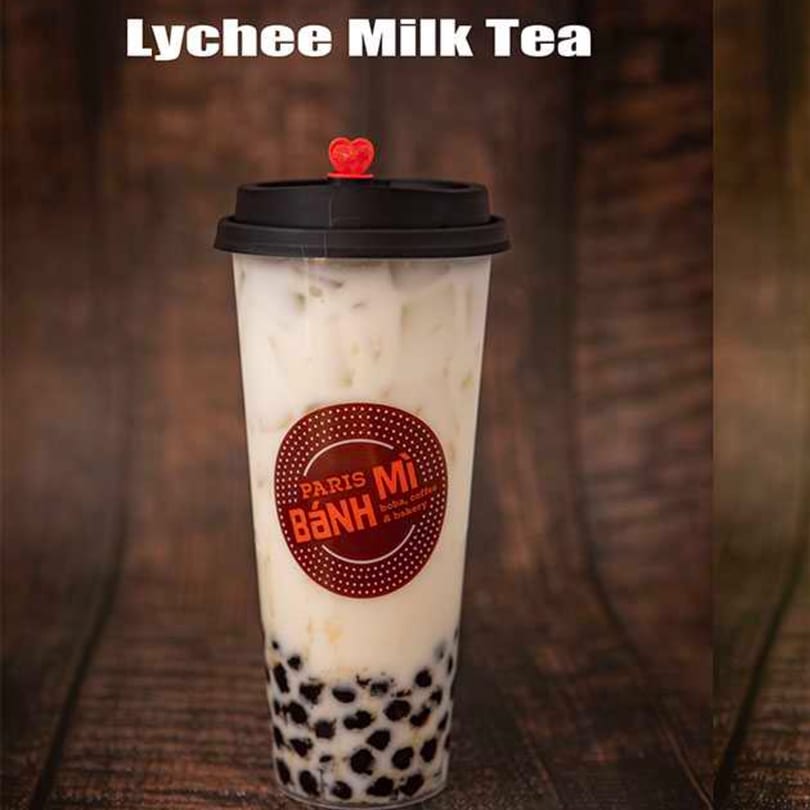 Lychee Milk Tea from Paris Banh Mi, a clear cup with white liquid, ice, and dark boba.